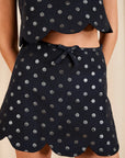 close up of a model wearing a dark colored top and skirt set with metallic polka dots on a cream background