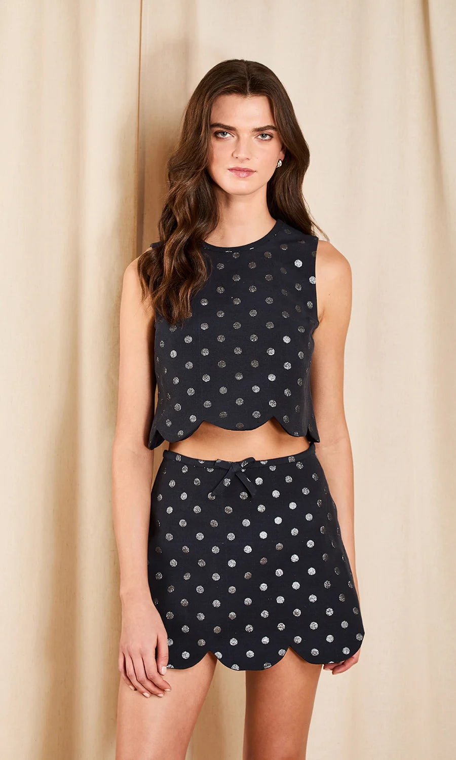 model wearing a dark colored top and skirt set with metallic polka dots on a cream background