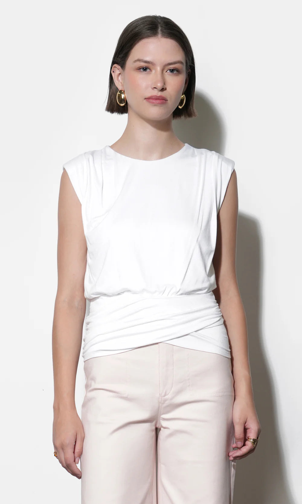 Woman wearing a white sleeveless top and light pink pants against a white background