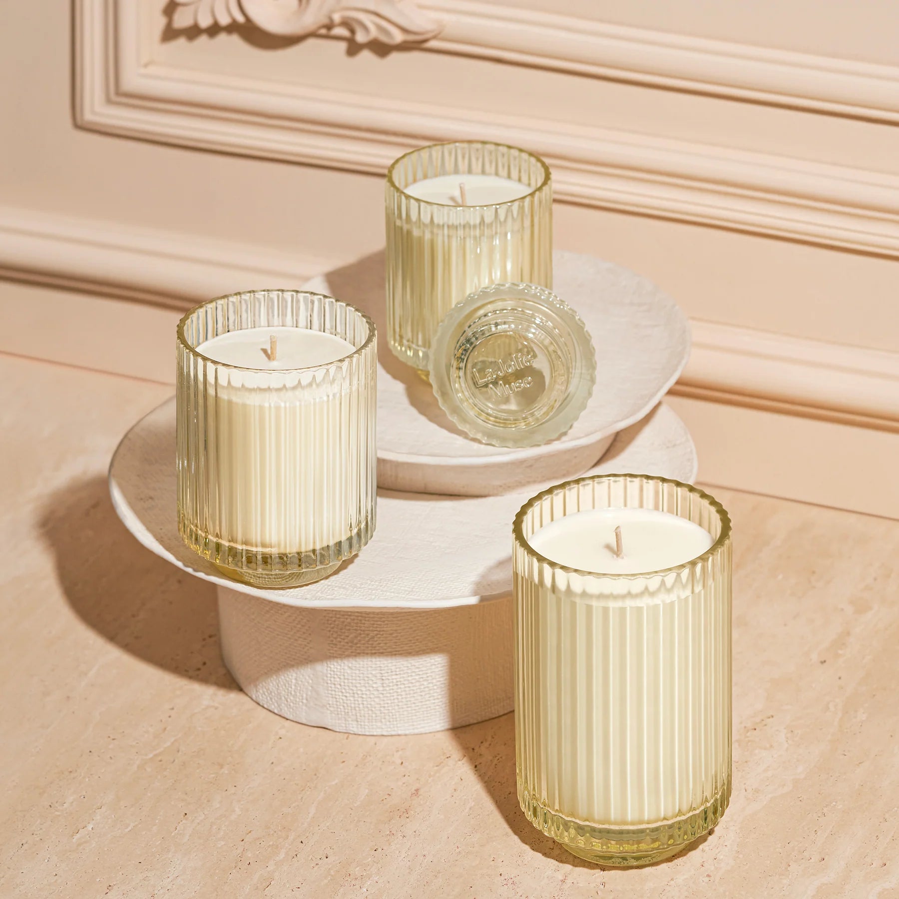 Three Champs de Tuberose Candles in glass holders on a decorative stand against a beige wall.
