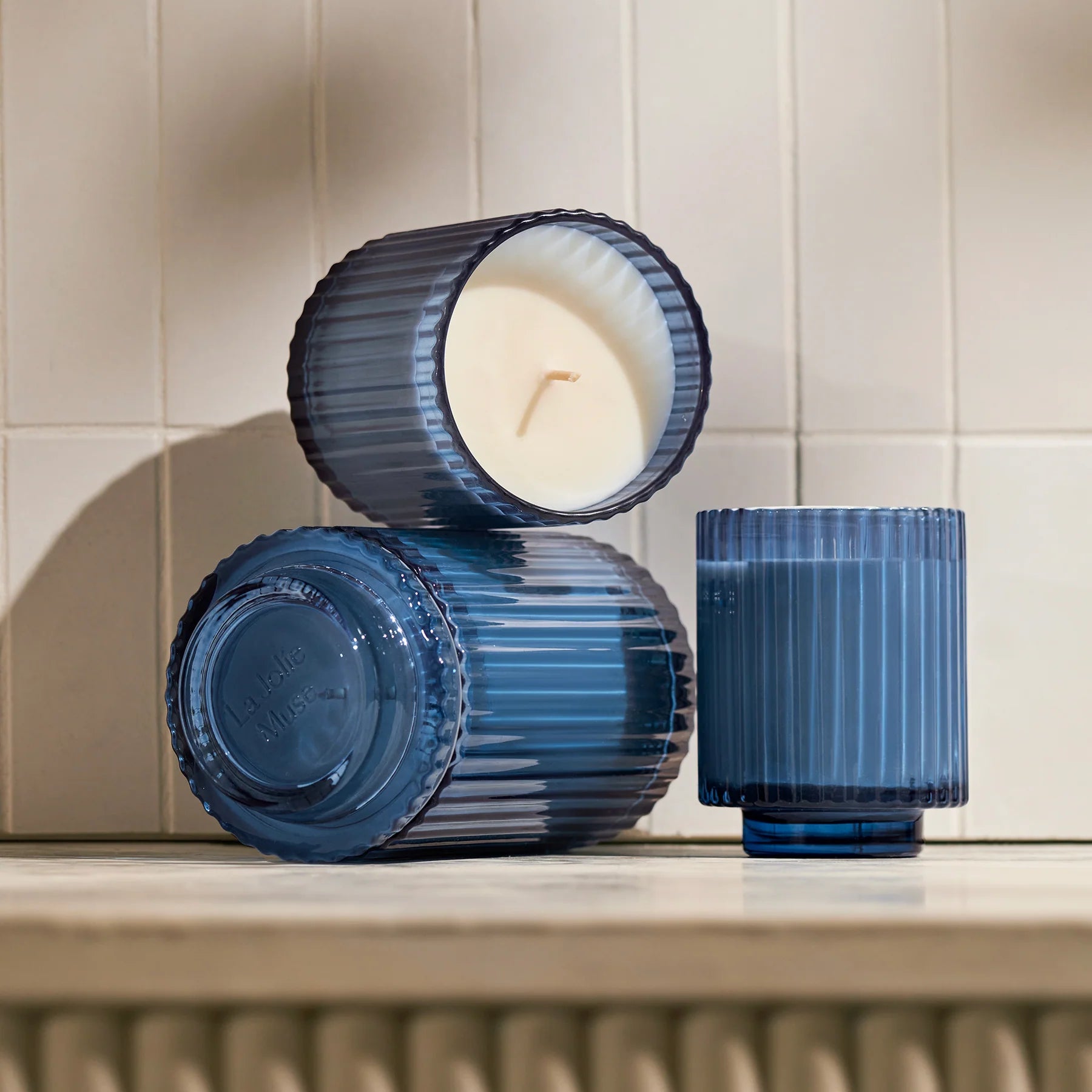 Two blue ribbed candle holders with a lit candle inside on a tiled wall background