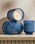 Two blue ribbed candle holders with a lit candle inside on a tiled wall background