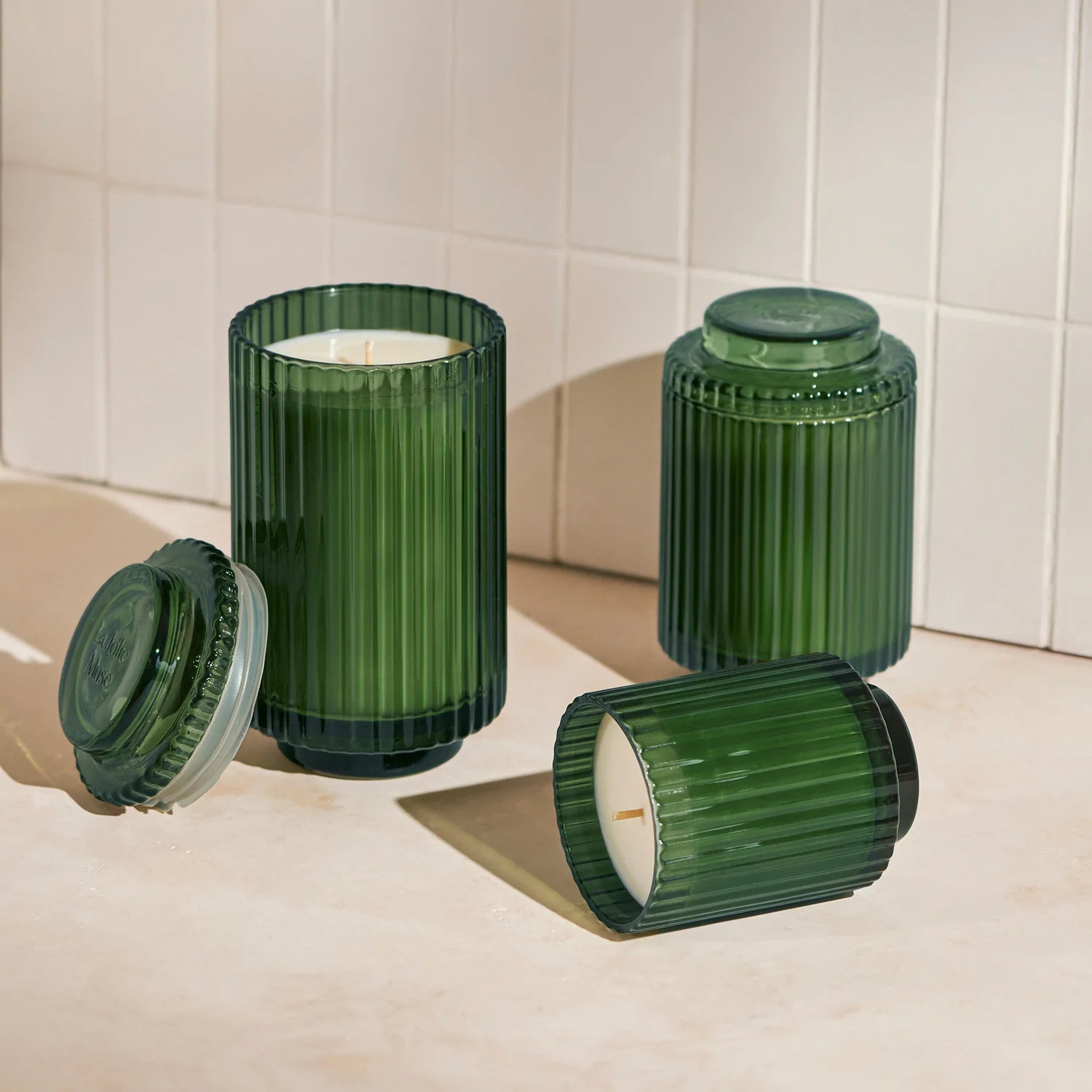 Green ribbed candle holders with candles on a tiled floor.