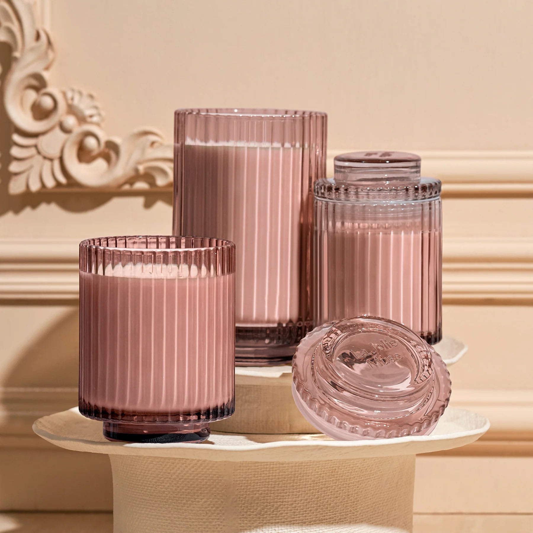 Set of pink glass containers on a decorative surface with a beige wall background