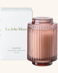 Pink scented candle with ribbed design and matching lid, next to its packaging box labeled 'La Jolie Muse'.