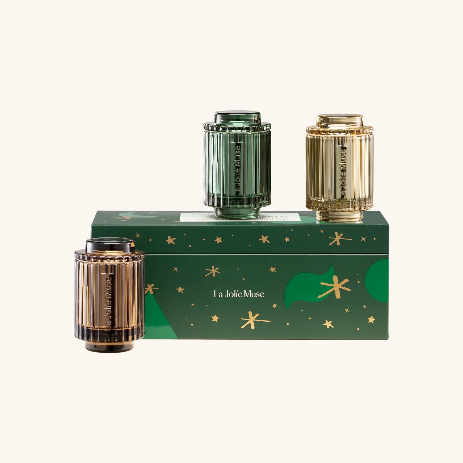 Three cylindrical containers with gold and green design on a green box labeled 'La Jolie Muse' against a white background.