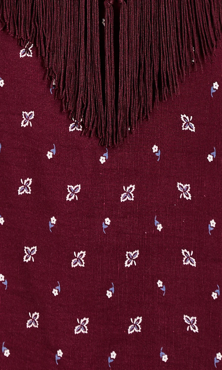 Close-up of a burgundy fabric with a fringe neckline and small white and blue floral embroidered motifs.
