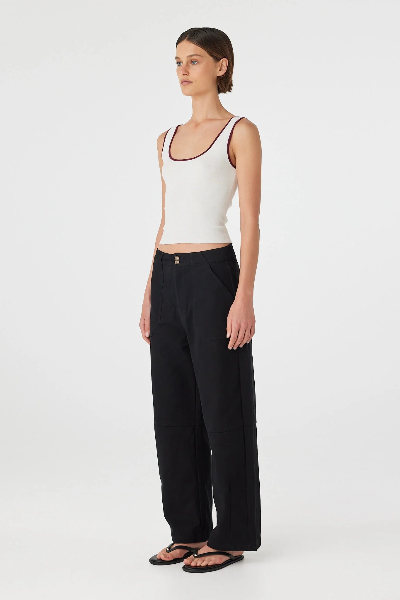 Woman wearing a white tank top and black pants on a white background