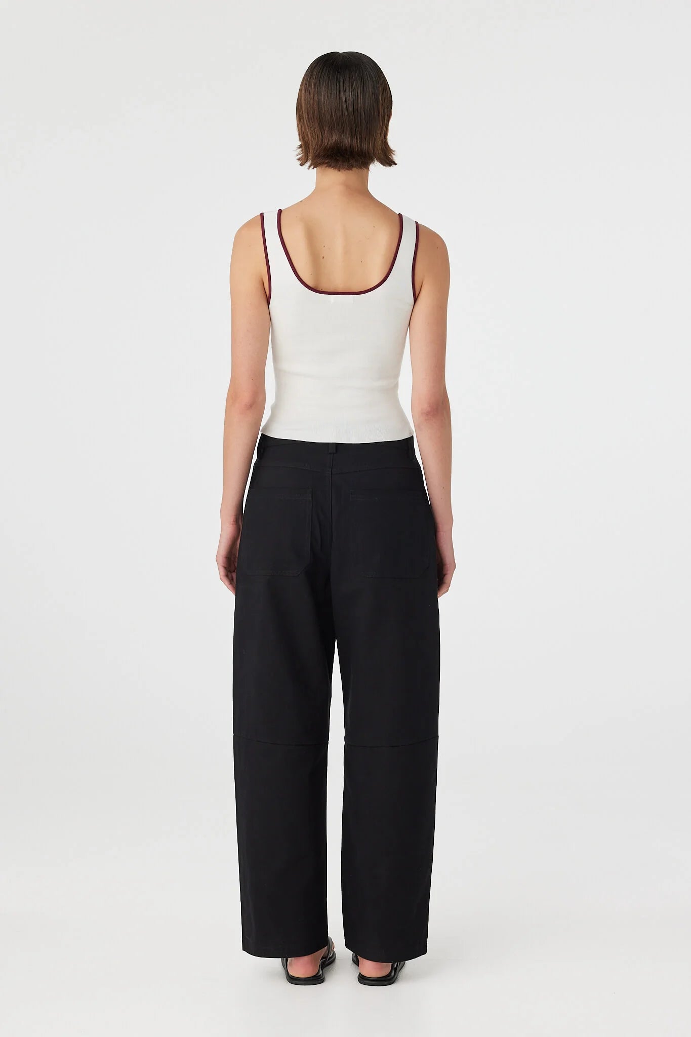 Person wearing a white tank top and black pants on a white background