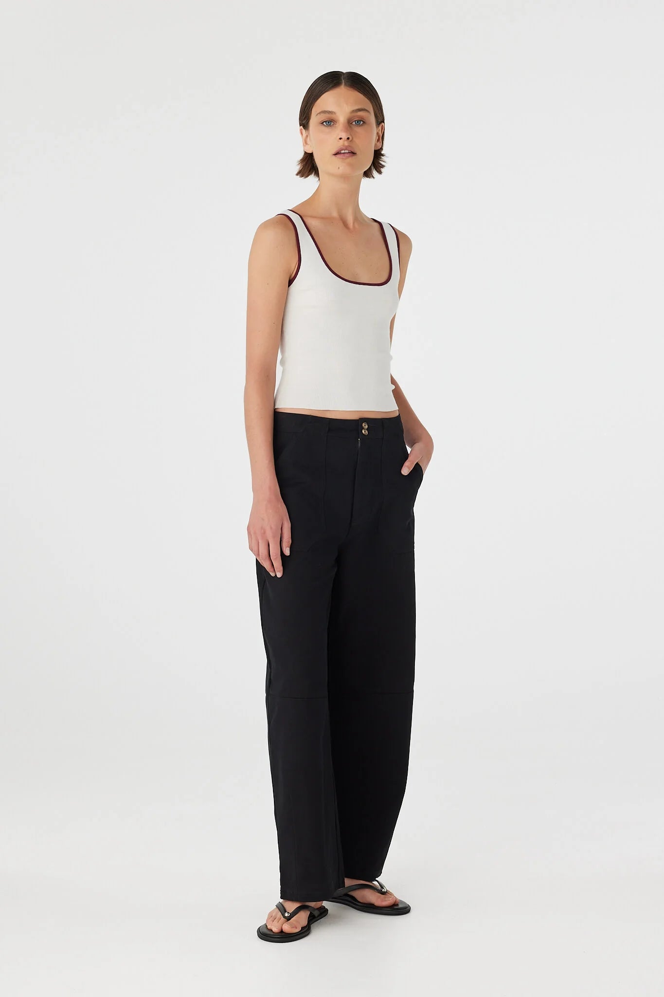 Woman wearing a white tank top and black pants on a white background