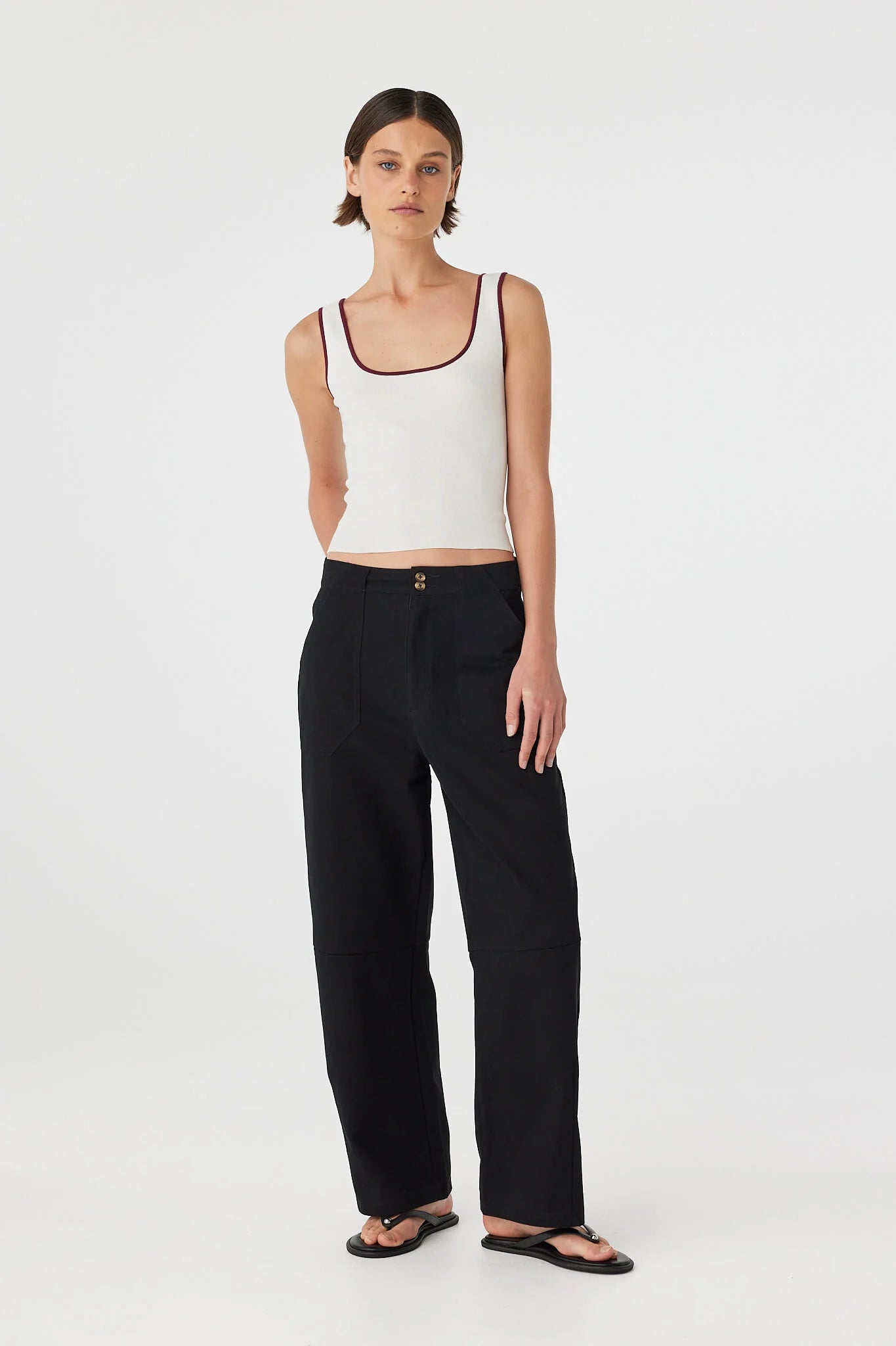 Woman wearing a white tank top and black pants on a white background