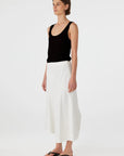Woman wearing a black tank top and white pants on a white background