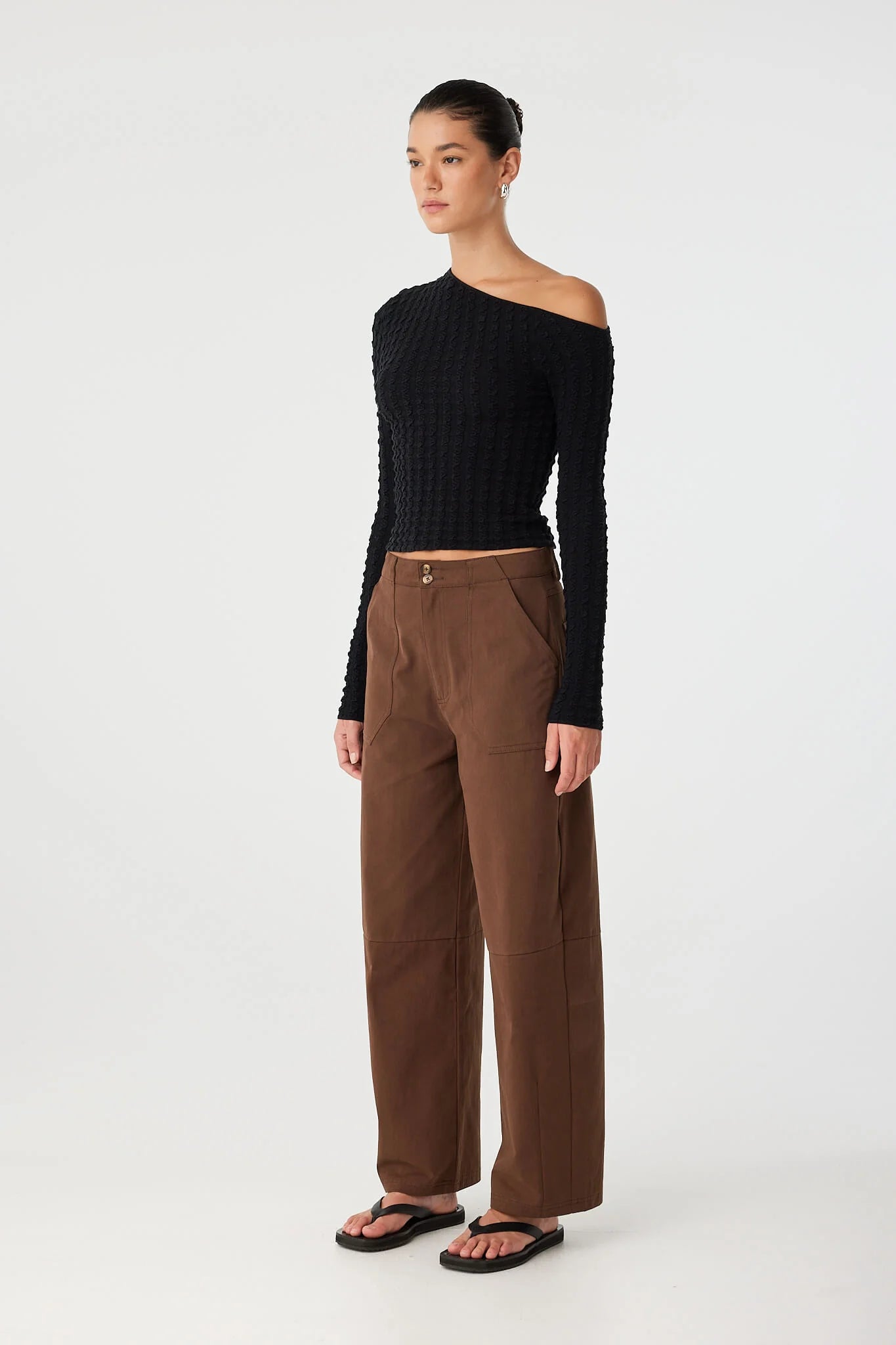 Person wearing a black off-shoulder top and brown pants on a white background
