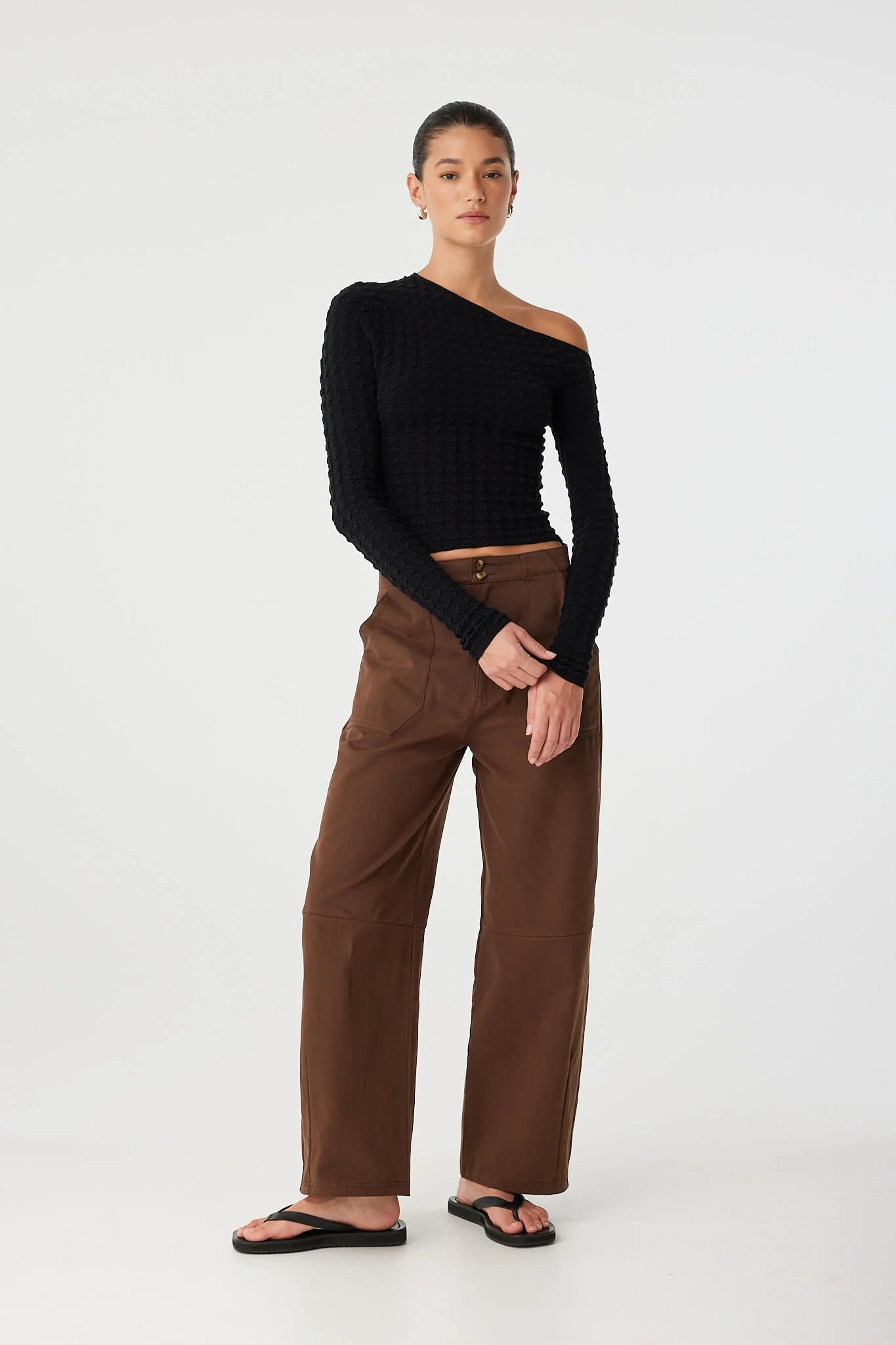 Woman wearing a black top and brown pants on a white background
