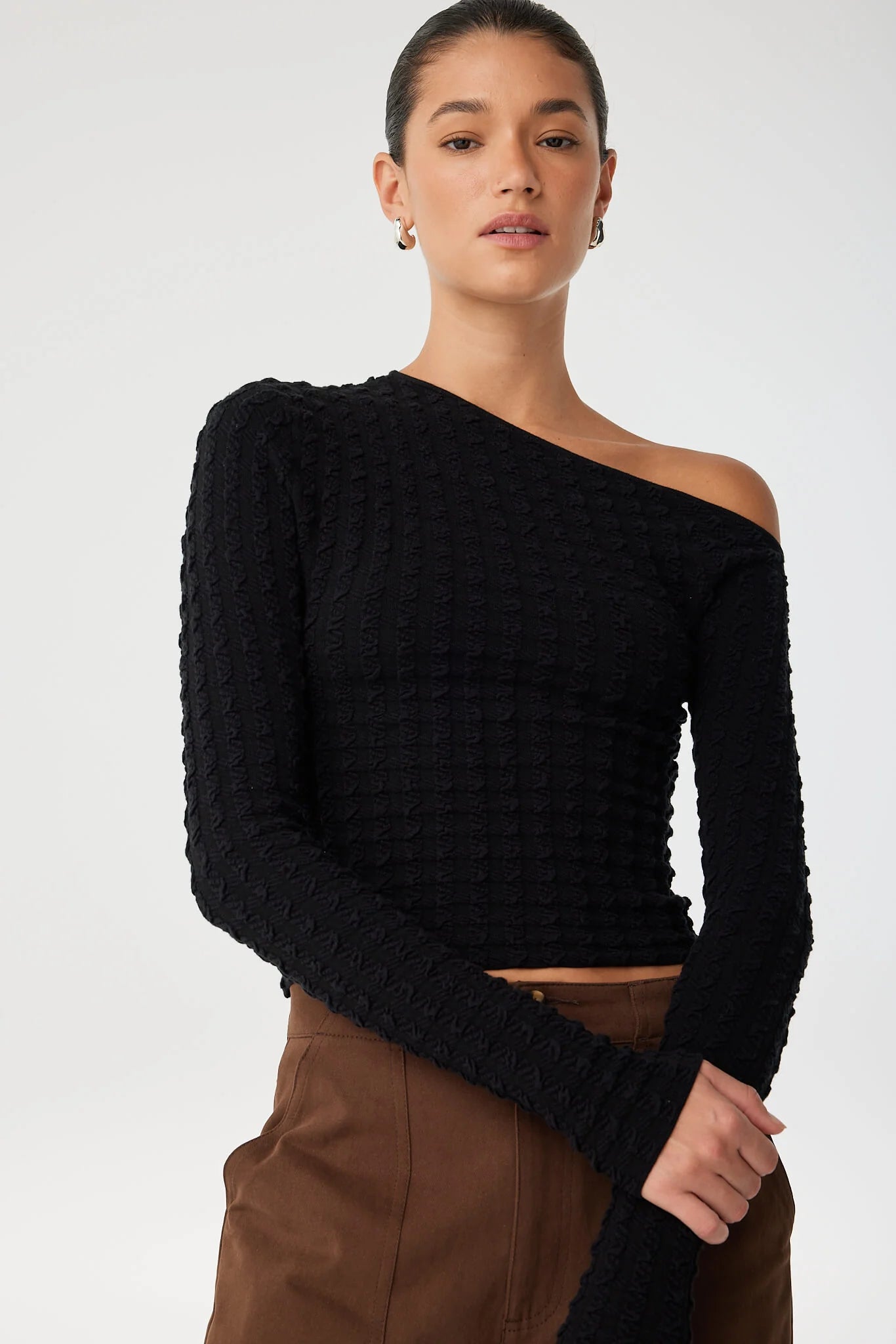 Woman wearing a black one-shoulder sweater against a white background