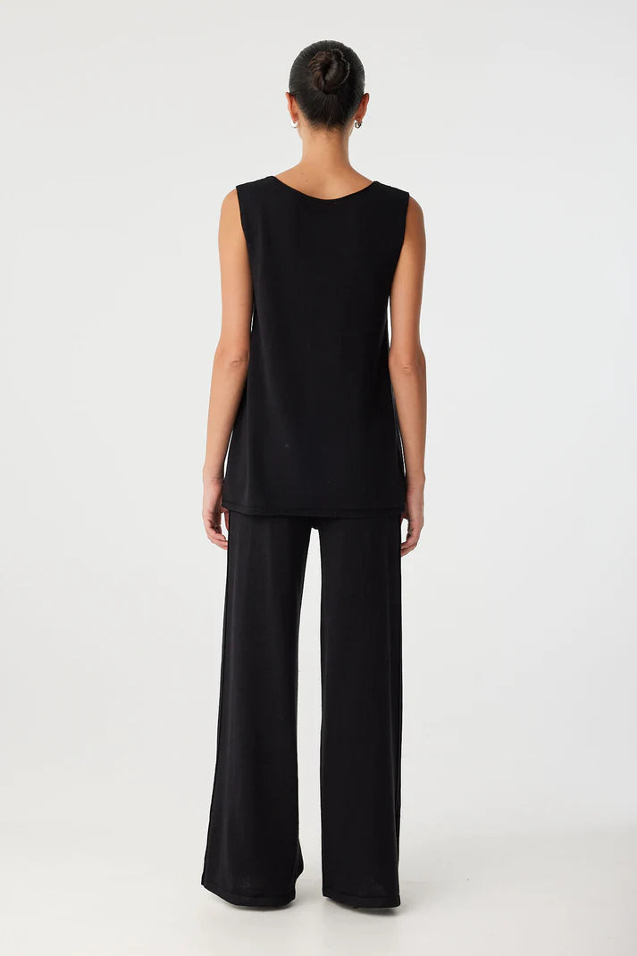 Person wearing a black sleeveless top and wide-leg pants on a white background, back