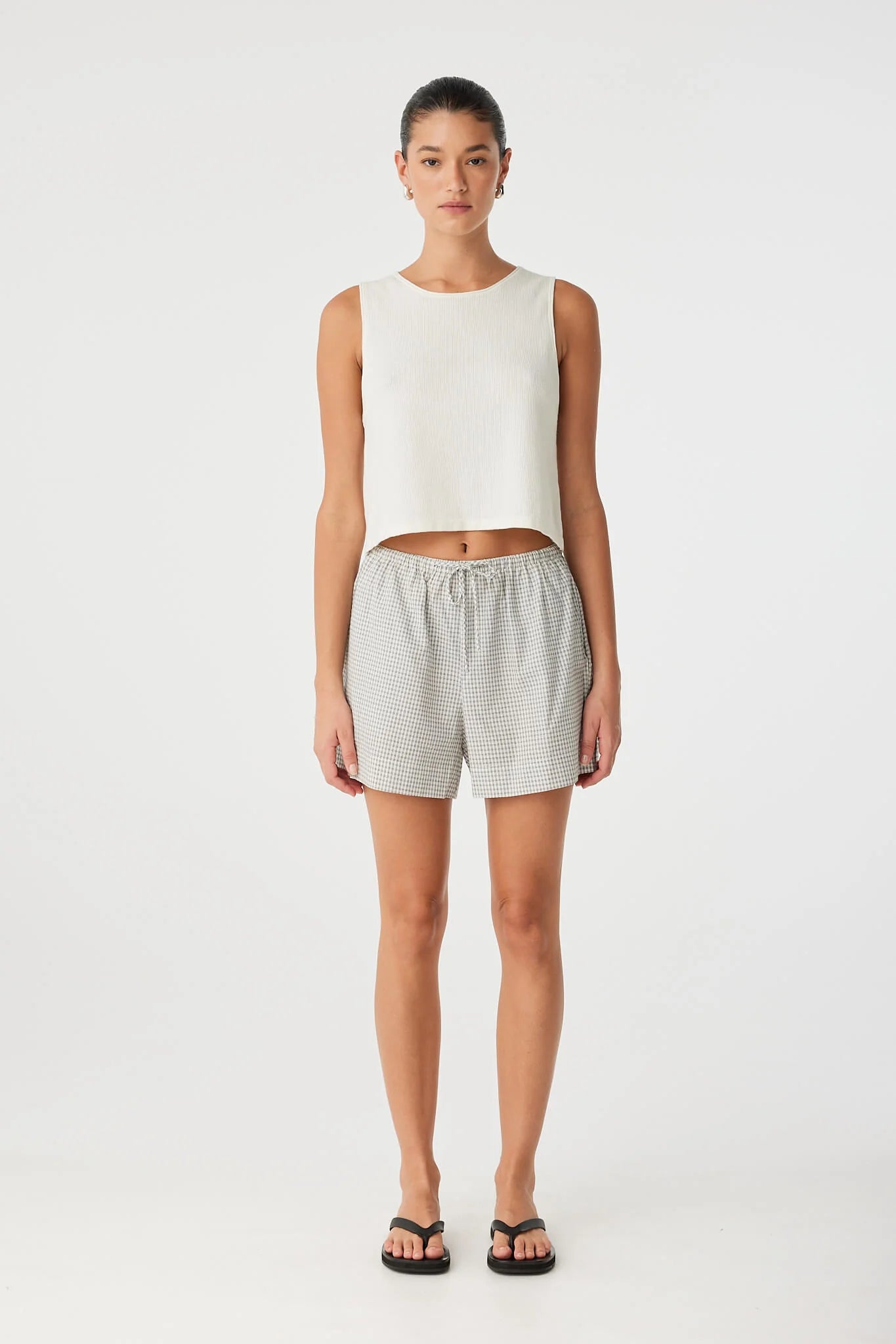 Woman wearing a white sleeveless top and gray shorts on a white background front