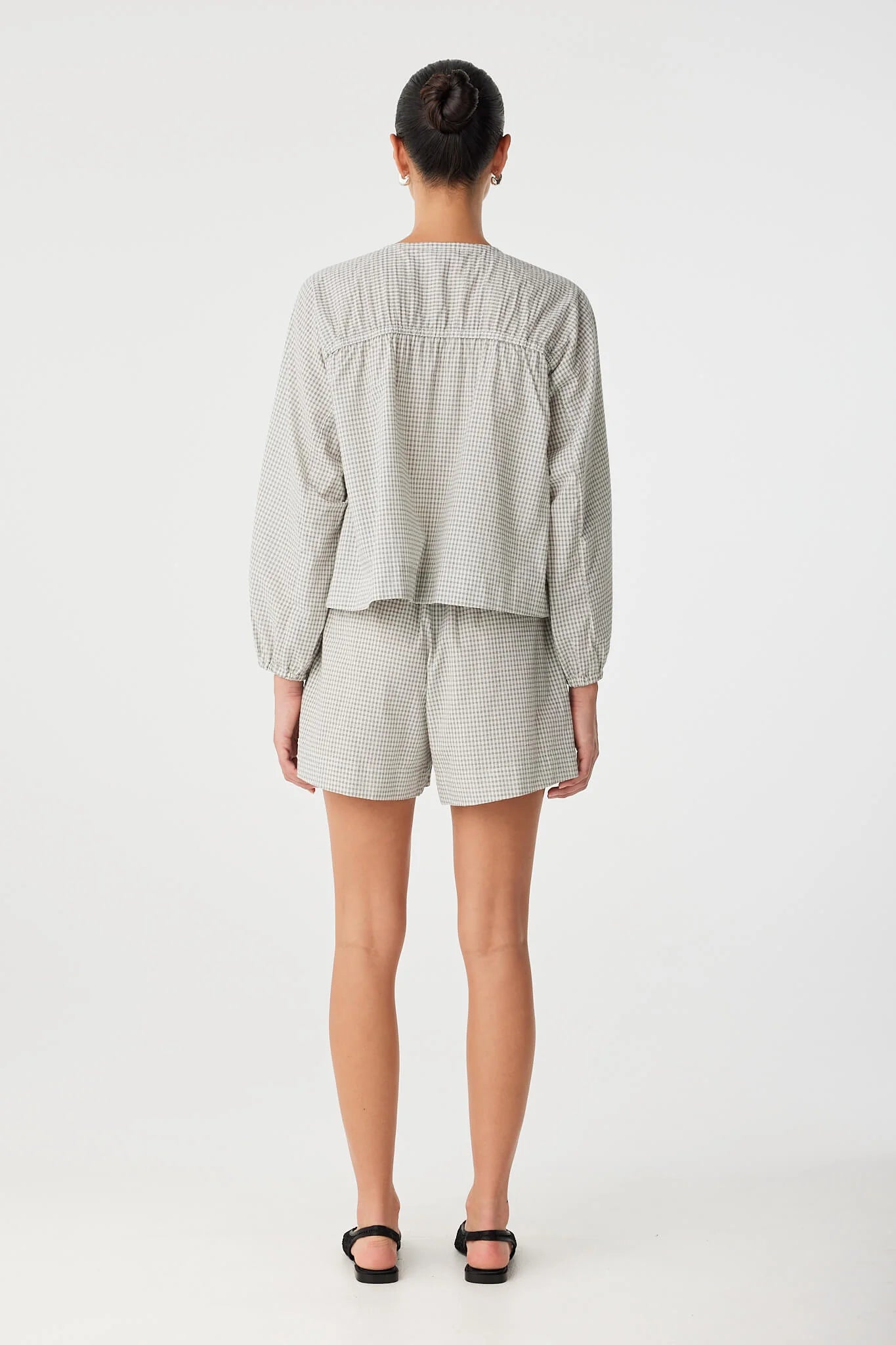Person wearing a light gray striped shirt and shorts on a white background back 