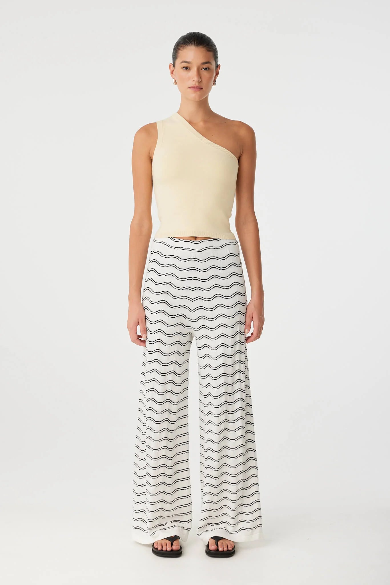 Woman wearing a one-shoulder top and striped pants on a white background
