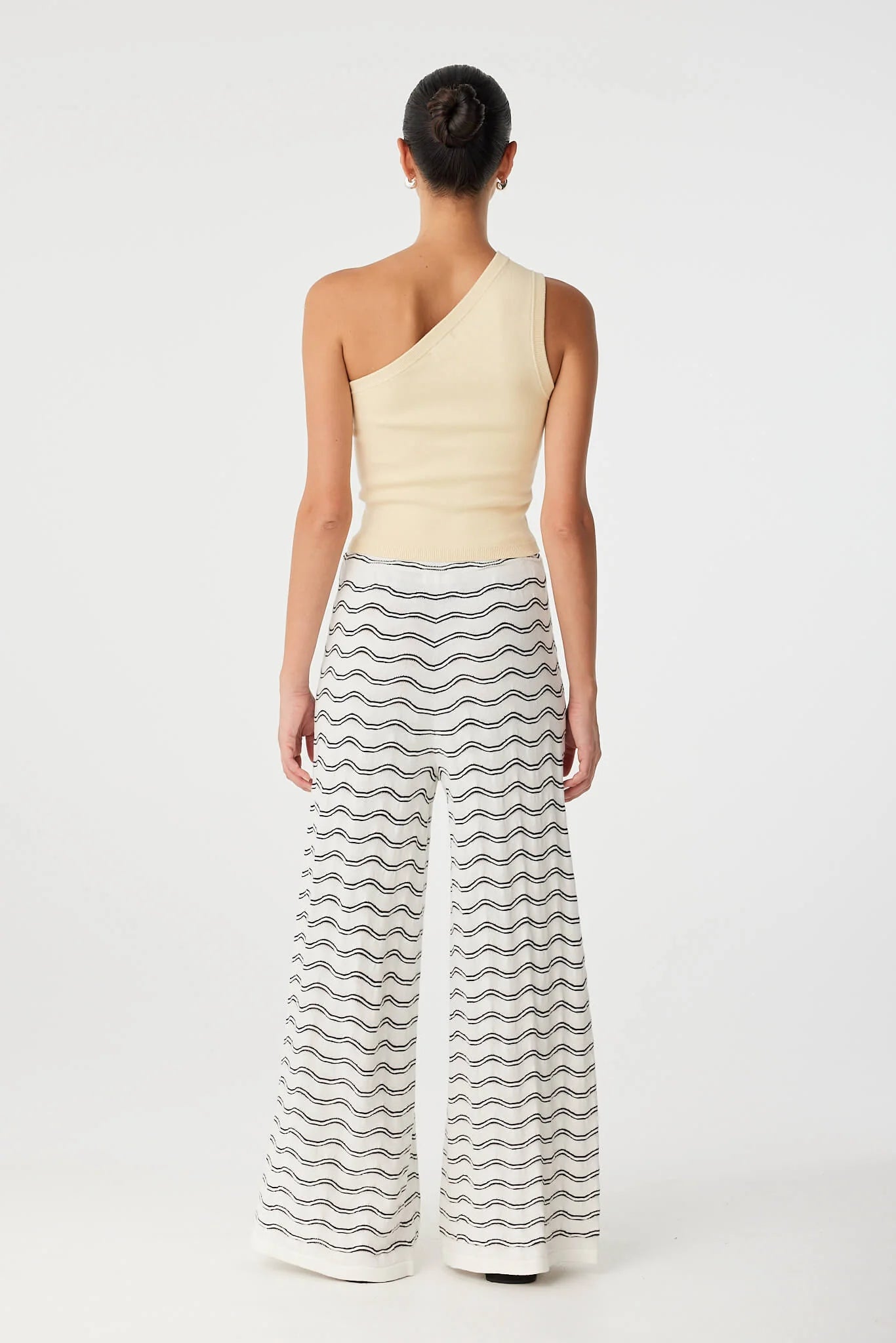 Woman wearing a one-shoulder top and wavy patterned pants on a white background