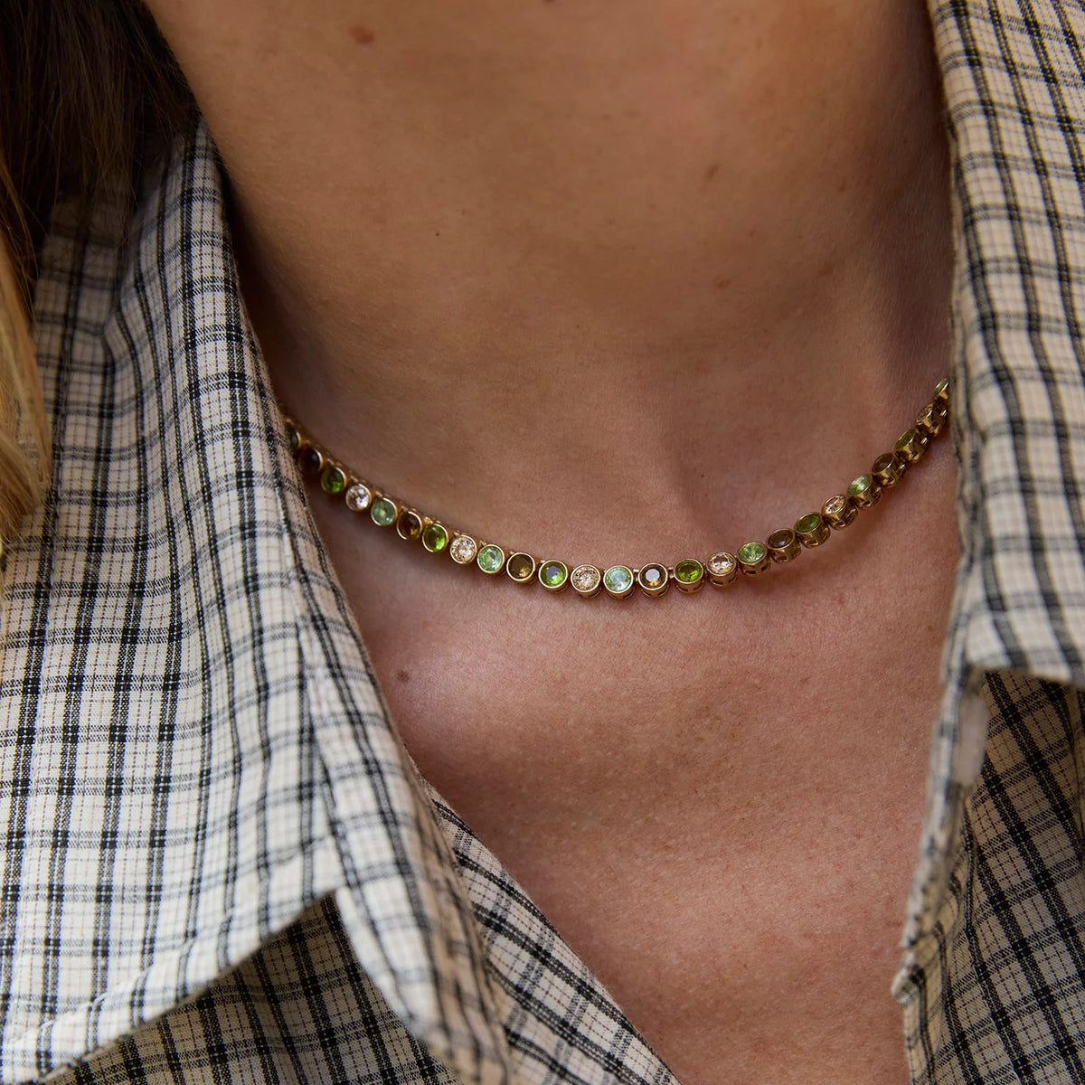 close up detail of a gold necklace with mixed colored stones on a model wearing a plaid shirt 