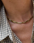 close up detail of a gold necklace with mixed colored stones on a model wearing a plaid shirt 