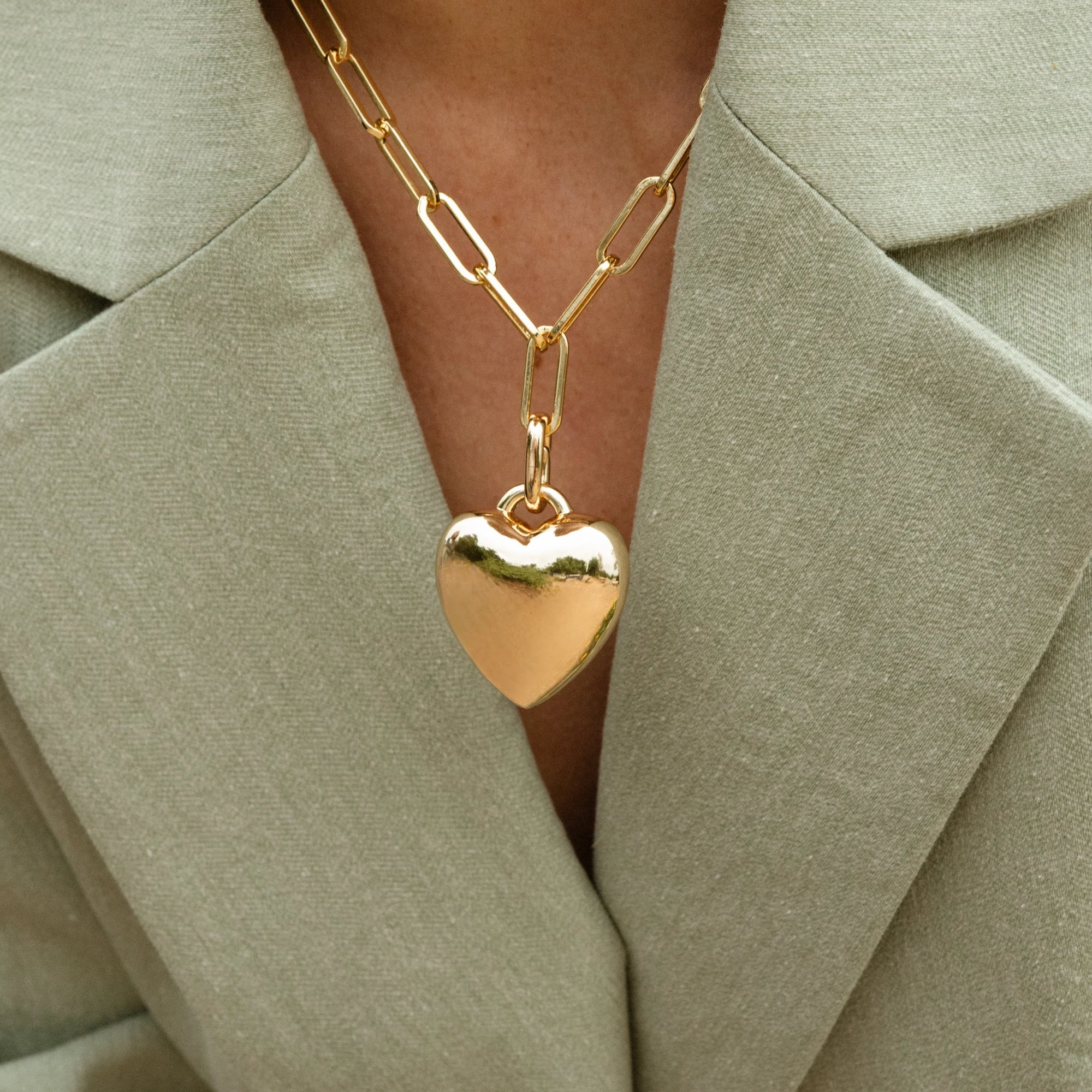 Gold heart-shaped pendant necklace on a person wearing a light green blazer.