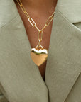 Gold heart-shaped pendant necklace on a person wearing a light green blazer.