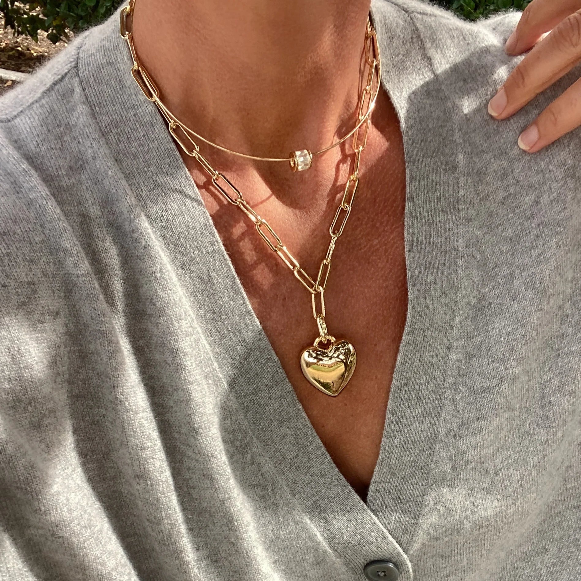 Close-up of a person wearing a gold chain necklace with a heart pendant.