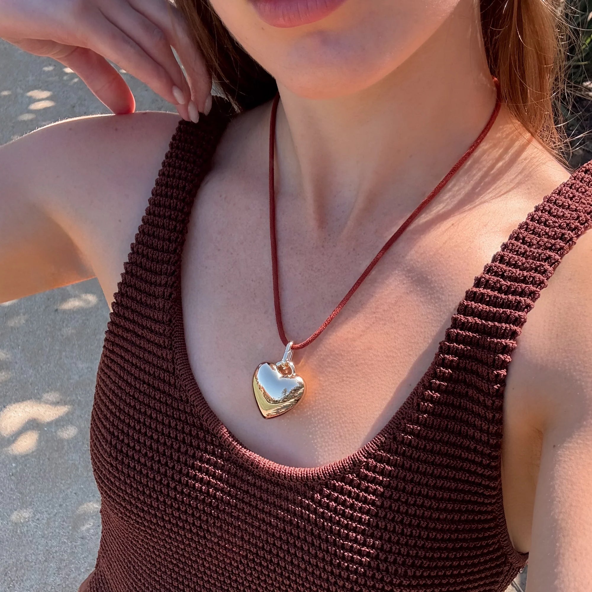 Woman wearing a brown textured top and a necklace with a heart pendant.