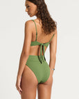 model wearing green bikini in beach setting, back view