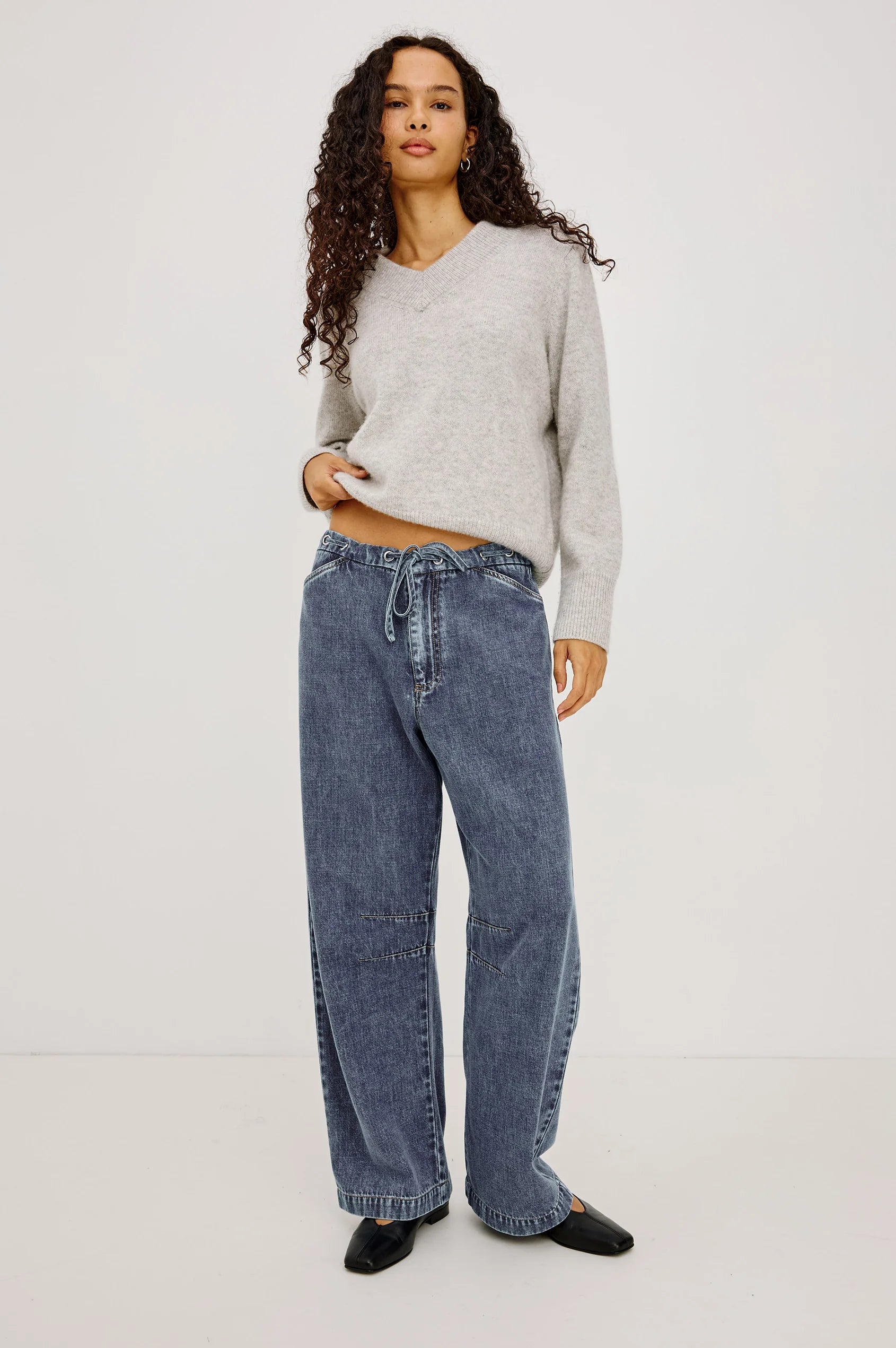 Woman wearing a gray sweater and blue jeans on a white background