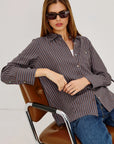 Woman wearing a striped shirt and sunglasses sitting on a chair with a white background