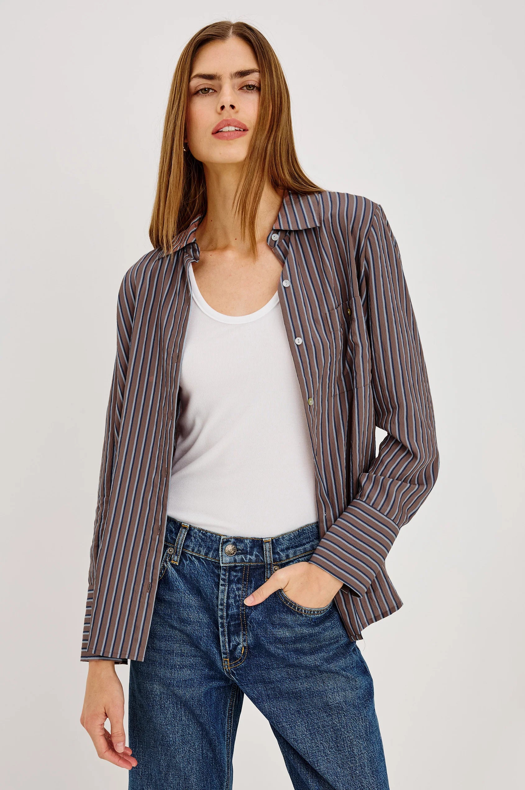 Woman wearing a striped shirt over a white top and jeans with a neutral background