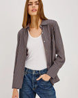 Woman wearing a striped shirt over a white top and jeans with a neutral background