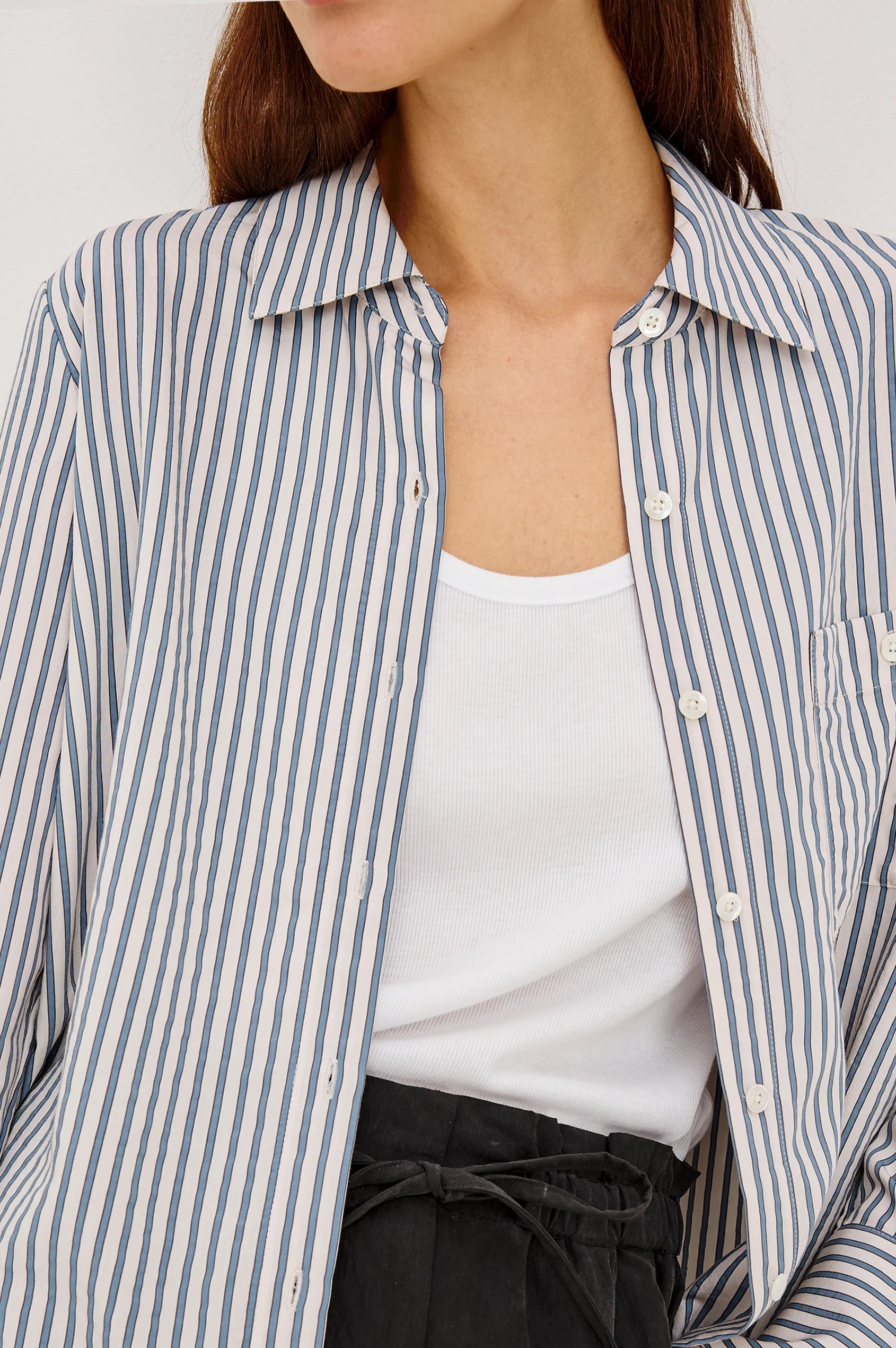Person wearing a striped shirt over a white top with a neutral background
