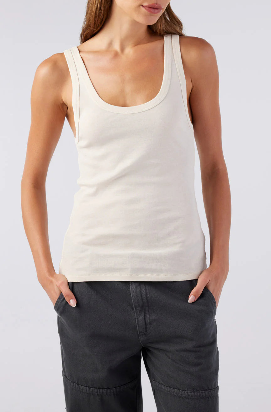 Woman wearing a white tank top and dark pants on a light gray background