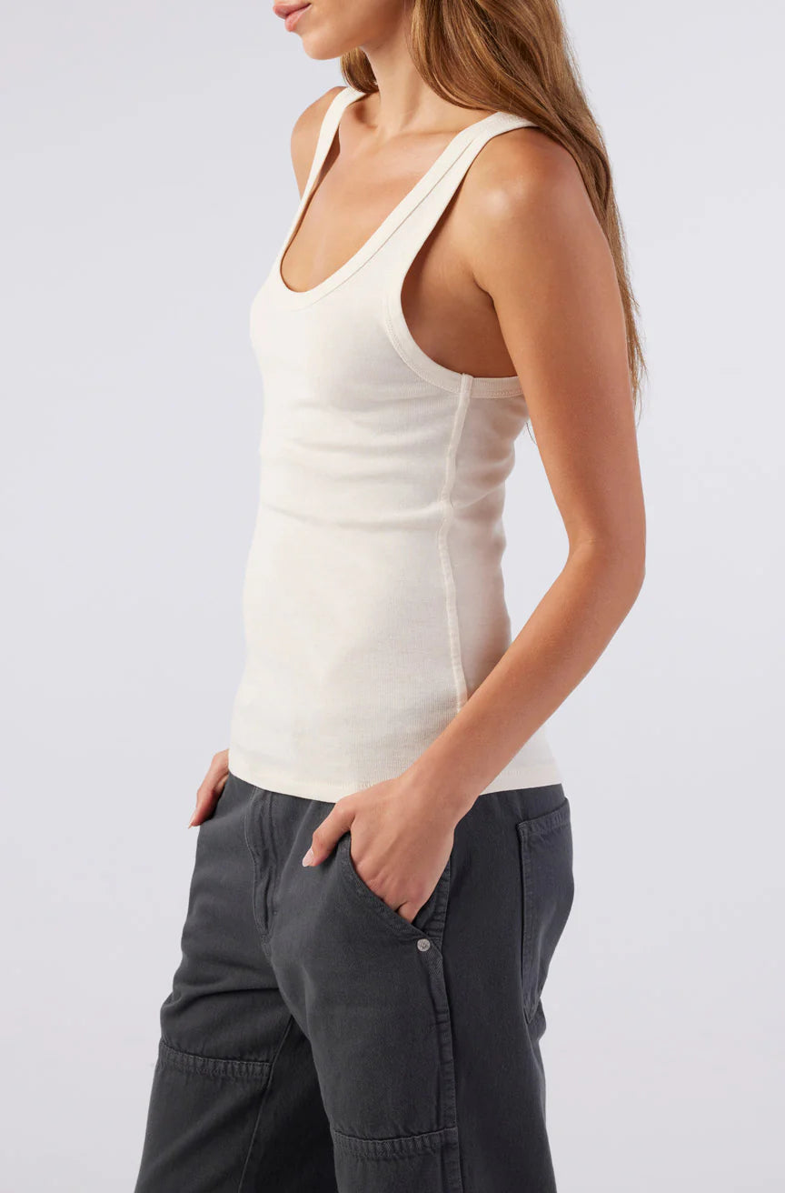 Woman wearing a white tank top and dark pants on a light gray background