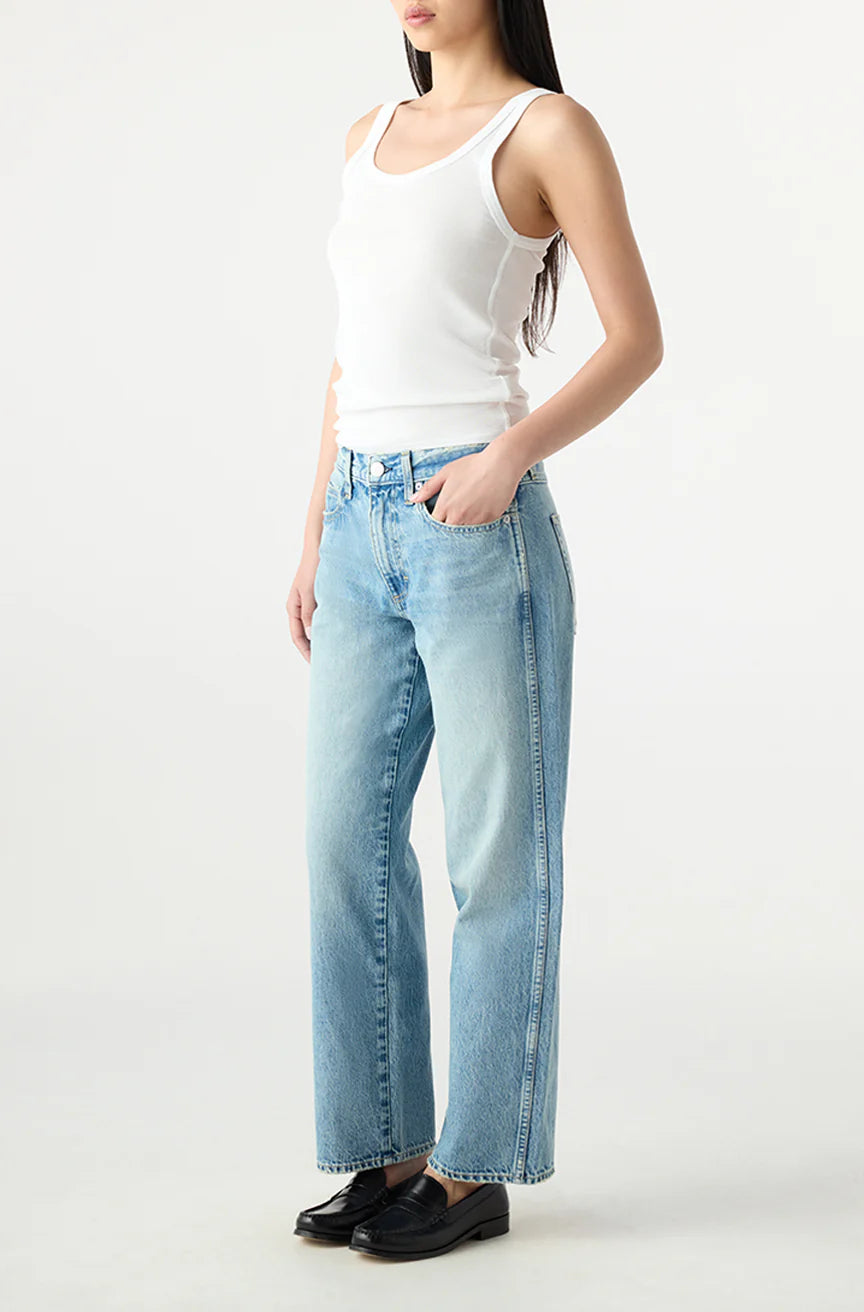 Person wearing a white tank top and light blue jeans on a white background, side