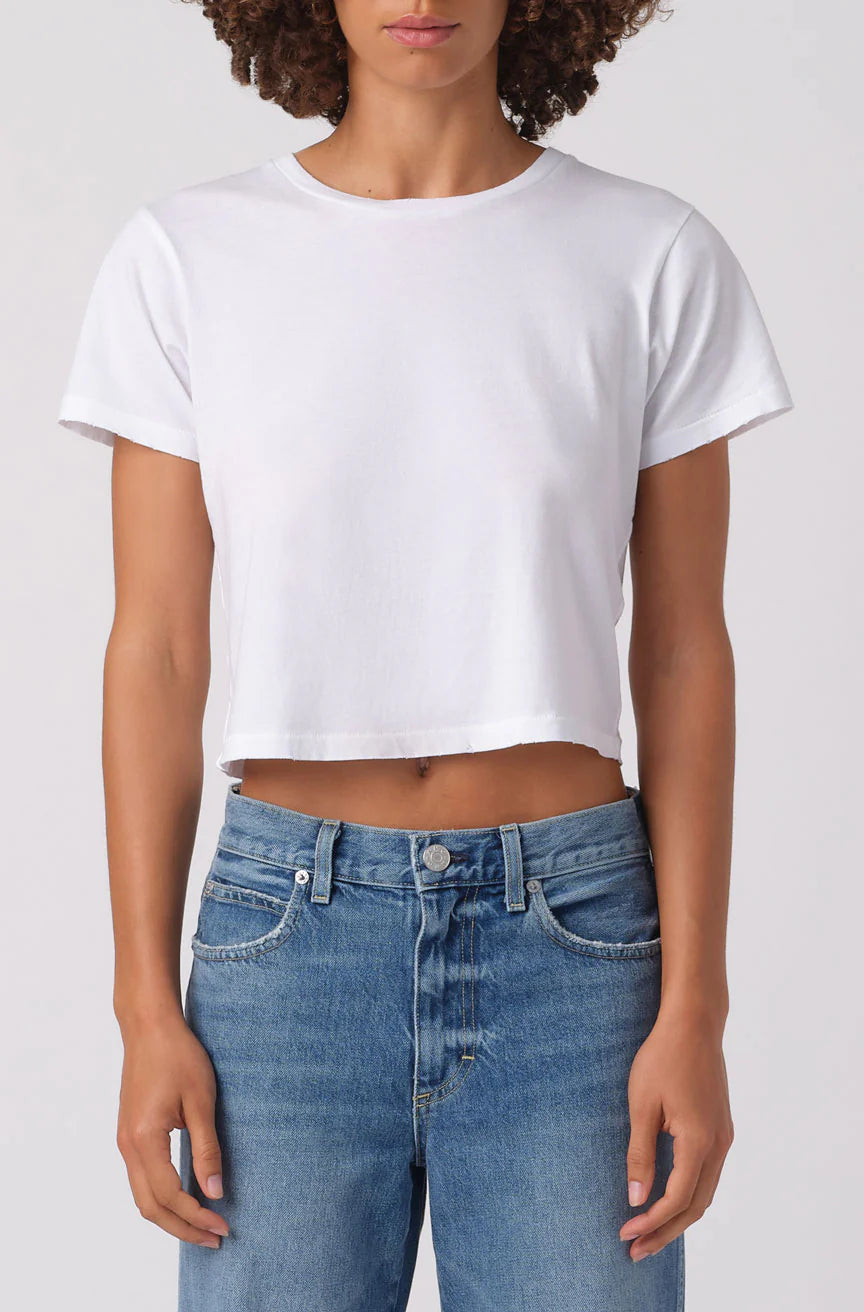 Person wearing a white crop top and blue jeans on a plain background