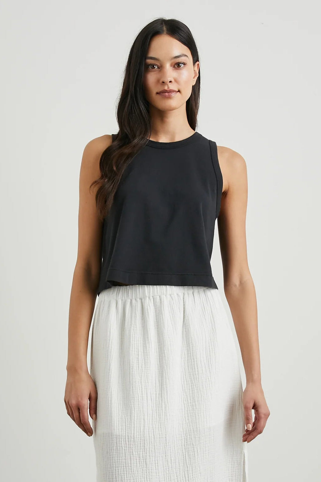 Woman wearing a black sleeveless top and white skirt against a plain background