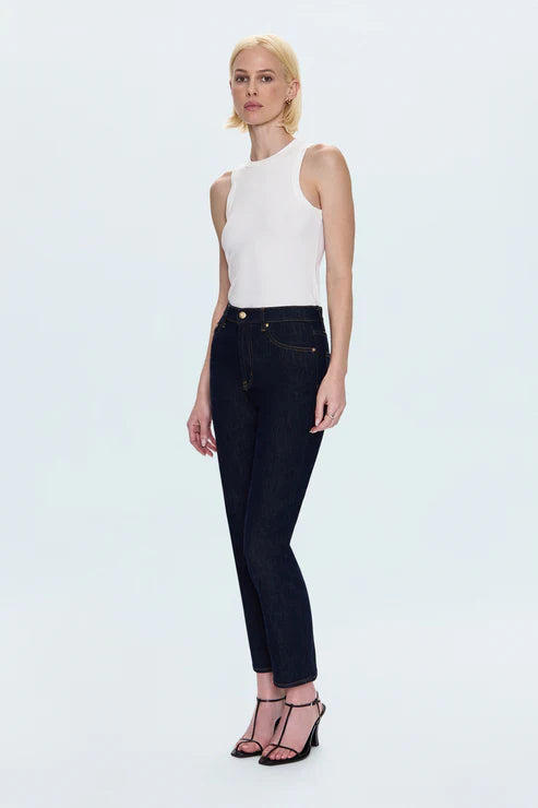 Woman wearing a white sleeveless top and dark jeans on a light blue background