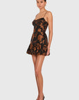 A model wearing a black and brown floral lace mini dress with spaghetti straps and a ruffled hem, paired with black pointed-toe heels, against a light gray studio background.