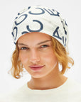 A close-up of a model wearing a white fabric headscarf with a navy blue abstract graphic pattern, set against a plain white background.