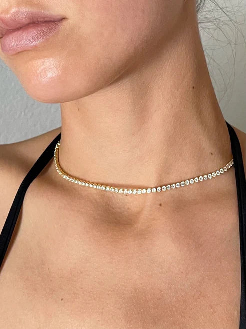 Close-up of a person wearing a delicate gold necklace with a neutral background