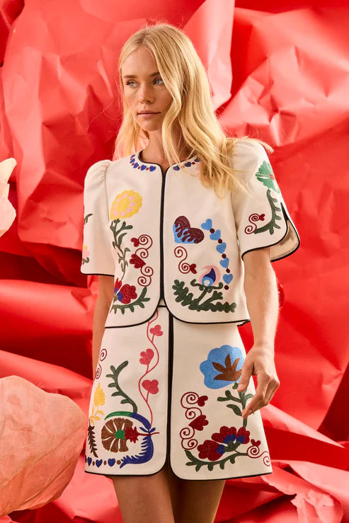 Woman wearing a white outfit with colorful floral patterns against a red background