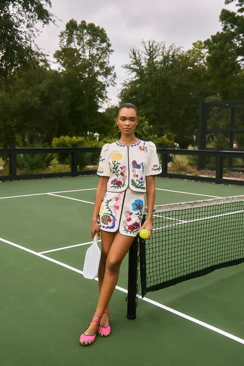 Woman in a floral outfit standing on a tennis court holding a racket and a ball.