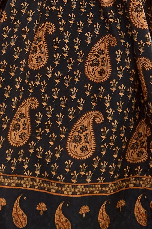 A close-up of a black fabric printed with a repeating tan paisley and floral block pattern, including a decorative border along the bottom edge.