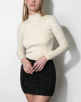 woman wearing a cream long sleeve top with a black mini skirt on a white background