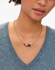 Gold necklace with colorful beads worn by a person in a blue sweater.